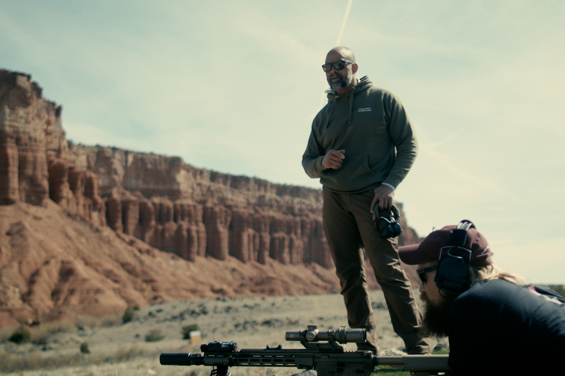 Instructor Buck Doyle teaching a student during an outdoor scoped carbine training class.<br />
Caption: Firearm instructor Buck Doyle provides real-time coaching and feedback during a long-range carbine clinic.
