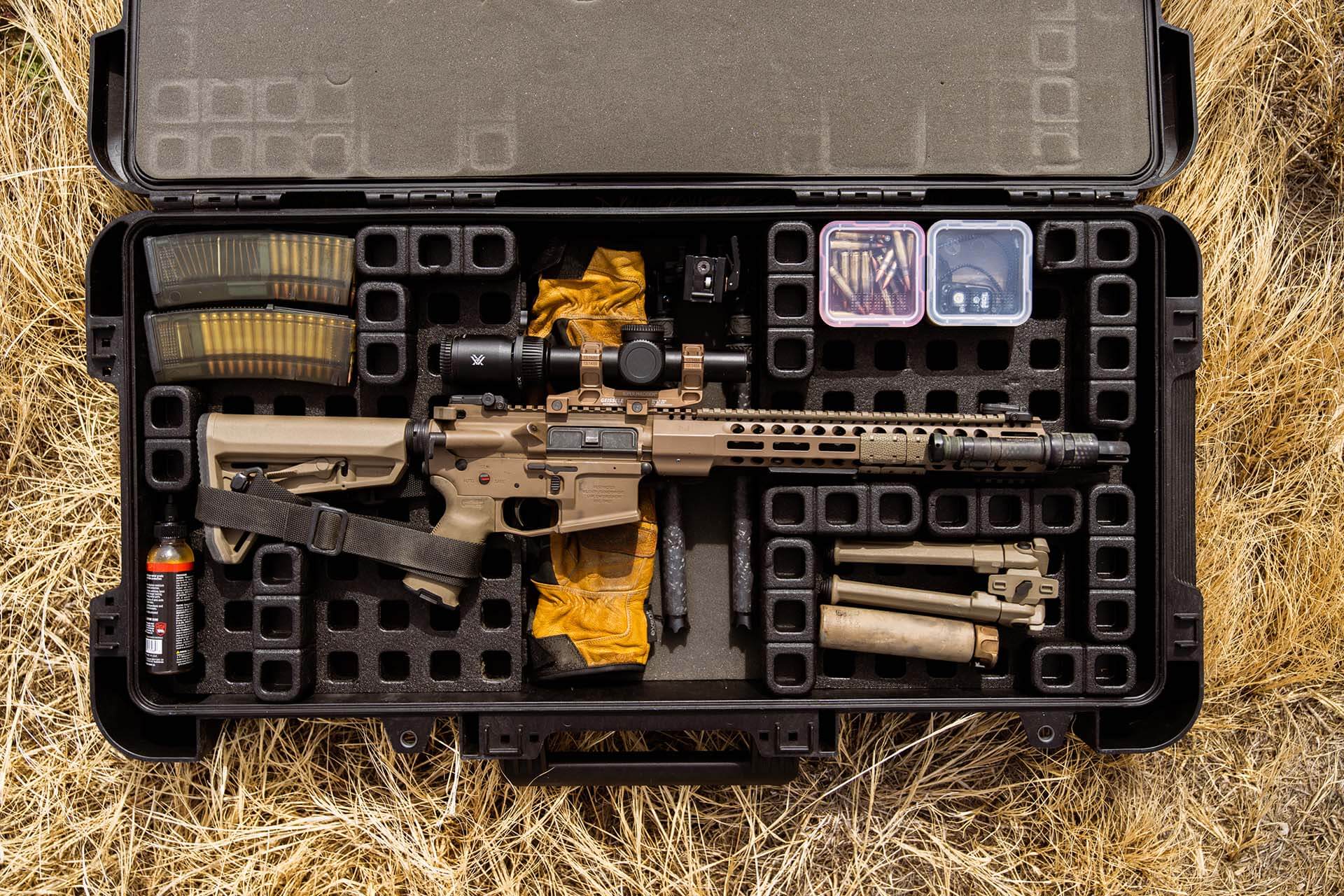 Flat dark earth AR15 rifle packed neatly inside a modular hard rifle case along with loaded magazines, gloves, and predator hunting gear.
